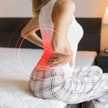 Person sitting on a bed holding their lower back